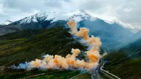 Via Global Times Clouds of colourful smoke rise from a fireworks display over hills, with the snow-capped peaks of the Himalayas in the distance