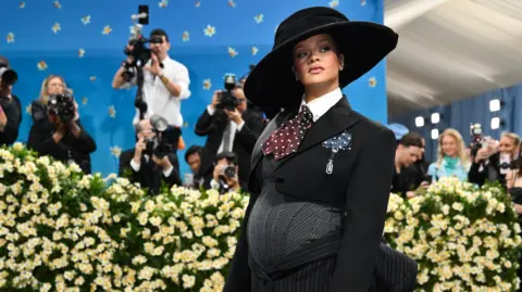 Getty Images Rihanna appears at the Met Gala wearing an outfit tailored to her pregnant stomach. Photographer stand behind a bank of daffodils to snap pictures of her.