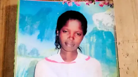 Wanjiru Family A photo of Agnes Wanjiru wearing a pink fleece top against a blue background.