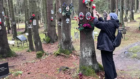 BBC A woman puts flowers on a tree in the woods outside St Petersburg where tens of thousands of Stalin's victims are buried