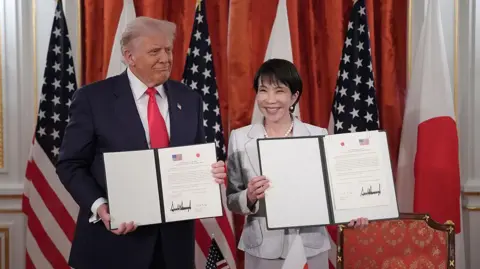 Getty Images US President Donald Trump (L) and Japanese Prime Minister Sanae Takaichi (R) hold up signed documents for an agreement toward a New Golden Age for the U.S.-Japan Alliance during a meeting at Akasaka Palace