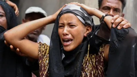 STR / EPA / Shutterstock A woman, holding her head, weeps, while a man behind her tries to comfort her