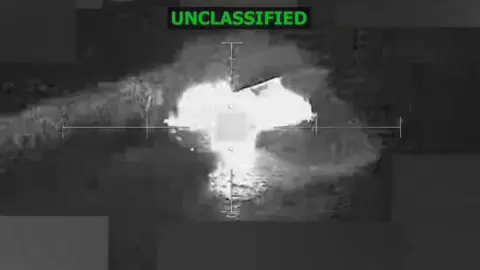 US Southern Command Still back-and-white image from a video showing a boat exploding into a fireball in the ocean with the word "unclassified" at the top