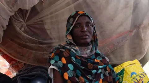 AFP via Getty Images A woman who has fled el-Fasher sits in a makeshift tent in a camp for displaced people.