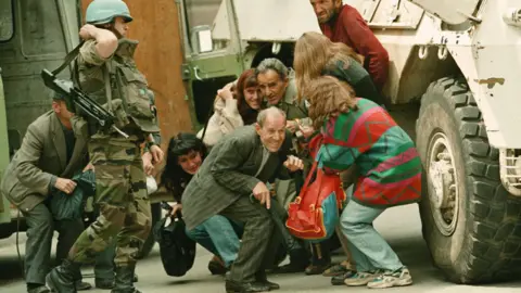 AP Photo/Jerome Delay A French U.N. soldier stands alongside a group of Sarajevans seeking shelter behind a French U.N. armoured personnel carrier from sniper-fire after being rescued from their van by French U.N. peacekeepers at a dangerous Sarajevo intersection Thursday June 8, 1995. 