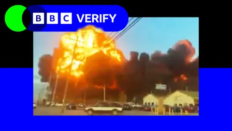 BBC A fireball erupts after the UPS cargo jet crash in Louisville, Kentucky. In the foreground cars are driving along a highway as the blast rages. 
