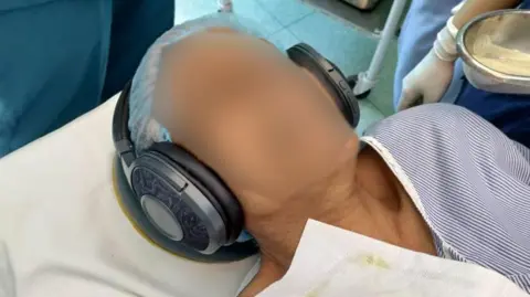 BBC A patient with headphones playing music during surgery in a hospital in Delhi