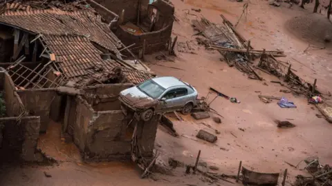 AFP via Getty Images An aerial view shows a partly destroyed house, with a car balancing on the roof, after a dam burst in the village of Bento Rodrigues, in Mariana, Brazil on 6 November 2015.