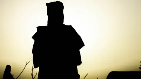 BBC Silhouettes of two people from Mali at M'berra refugee camp in Mauritania as the sun is low in the sky