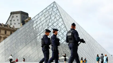 Reuters Three security guards walk in a row in front of the glass triangle structure of the Louvre