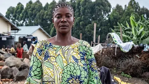 AFP via Getty Images A head and shoulders image of Congolese refugee Akilimali Mirindi after arriving at a refugee camp in Rwanda. She is wearing a yellow and green patterned dress. 