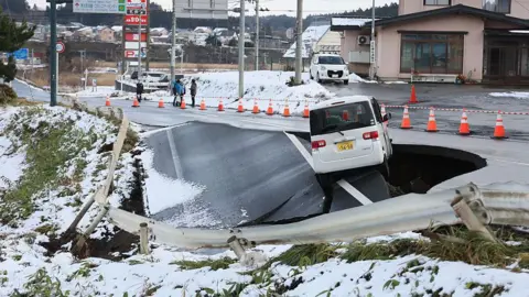 AFP via Getty Images A vehicle rests on the edge of a collapsed road in Tohoku town in Aomori Prefecture on December 9, 2025, following a 7.5 magnitude earthquake off northern Japan