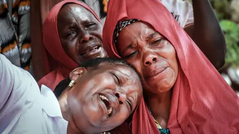 AFP via Getty Images A close-up of three distressed female mourners. They are crying as they attend stand over a coffin - unseen in the picture.