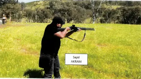 Supplied A man dressed in black and standing in a field of lush grass aims a shotgun
