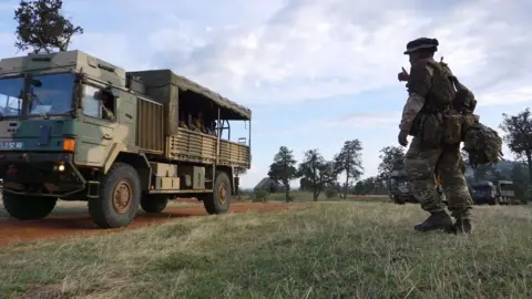 AFP via Getty Images A soldier wearing military attire gestures at a military lorry 