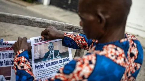 AFP via Getty Images A vendor arranges his newspaper display in Benin a day after the attempted coup. "Patrice Talon reassures the country", reads the headline on one.