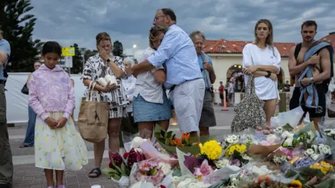 Reuters People in summer clothes mourn near floral tributes placed for victims and survivors of a deadly mass shooting