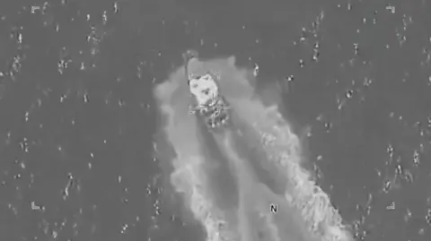 US Southern Command A greyscale aerial image shows a small boat speeding through a stretch of water, with a small square of focus visible in the centre.