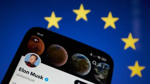 Getty Images A picture of a phone against the backdrop of the blue and yellow EU flag with yellow stars. The phone has Elon Musk's X profile on it with his face and a blue tick next to it. 
