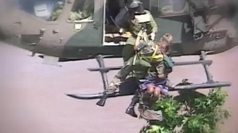 SABC An army medic attached to a helicopter passes a woman to someone on the aircraft.