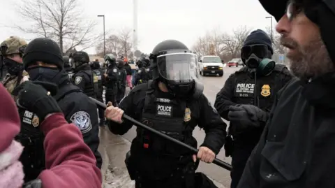 Reuters a Customs and Border Patrol agent holding up a baton as more agents gather behind him