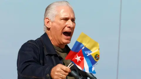 EPA/Shutterstock Cuban President Miguel Díaz-Canel holds Cuban and Venezuelan flags as he speaks at a rally in Havana in support of Venezuela. Photo: 3 January 2026