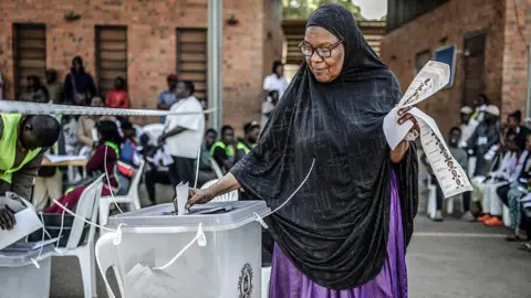 AFP via Getty Images A voter in a black headscarf places her vote in a ballot box.