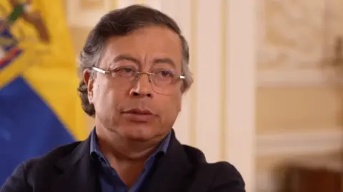 BBC Colombia's President Gustavo Petro wears a serious expression. He is dressed in a dark blue shirt and wears spectacles. 