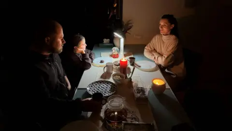BBC A family sits around a table in the dark