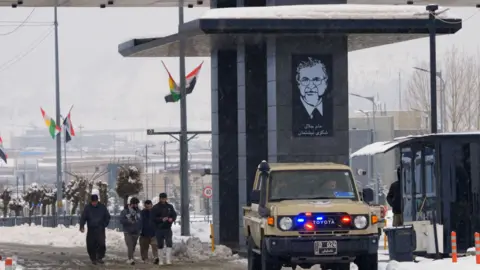 BBC Scene at Iraqi border with Iran, as a vehicle and people pass through a crossing point in the snow