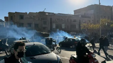 EPA A street-view image of Iranian shopkeepers and traders protesting on motorbikes and on foot in between cars with tear gas is visible.