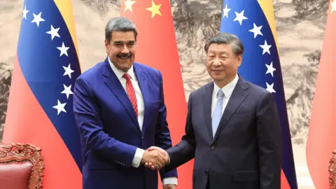 Miraflores Palace via Reuters Venezuelan president Nicolás Maduro (L) and Chinese president Xi Jinping shake hands and smile in front of Venezuelan and Chinese flags at the palace in Beijing in 2023.