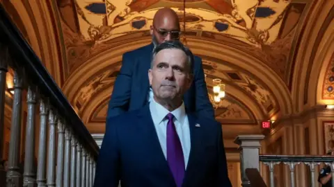 Reuters CIA director John Ratcliffe walks down a flight of stairs. A man with a bald head and glasses walks behind him. 