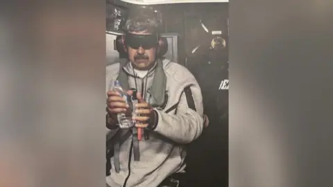 @realdonaldtrump Maduro on the USS Iwo Jima, wearing a grey tracksuit and holding a bottle of water. He is blindfolded and wearing ear protection.